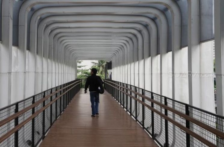 Pejalan kaki melintas di jembatan penyeberangan orang (JPO) Pasar Minggu, Jakarta, Rabu (22/1).[Suara.com/Angga Budhiyanto]